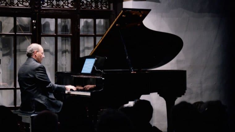 Mauricio Nader de perfil, tocando un piano de cola ante el público.